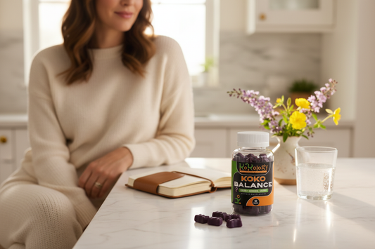 Koko Balance bottle in sharp focus with softly blurred dark purple bear gummies and botanicals on marble counter
